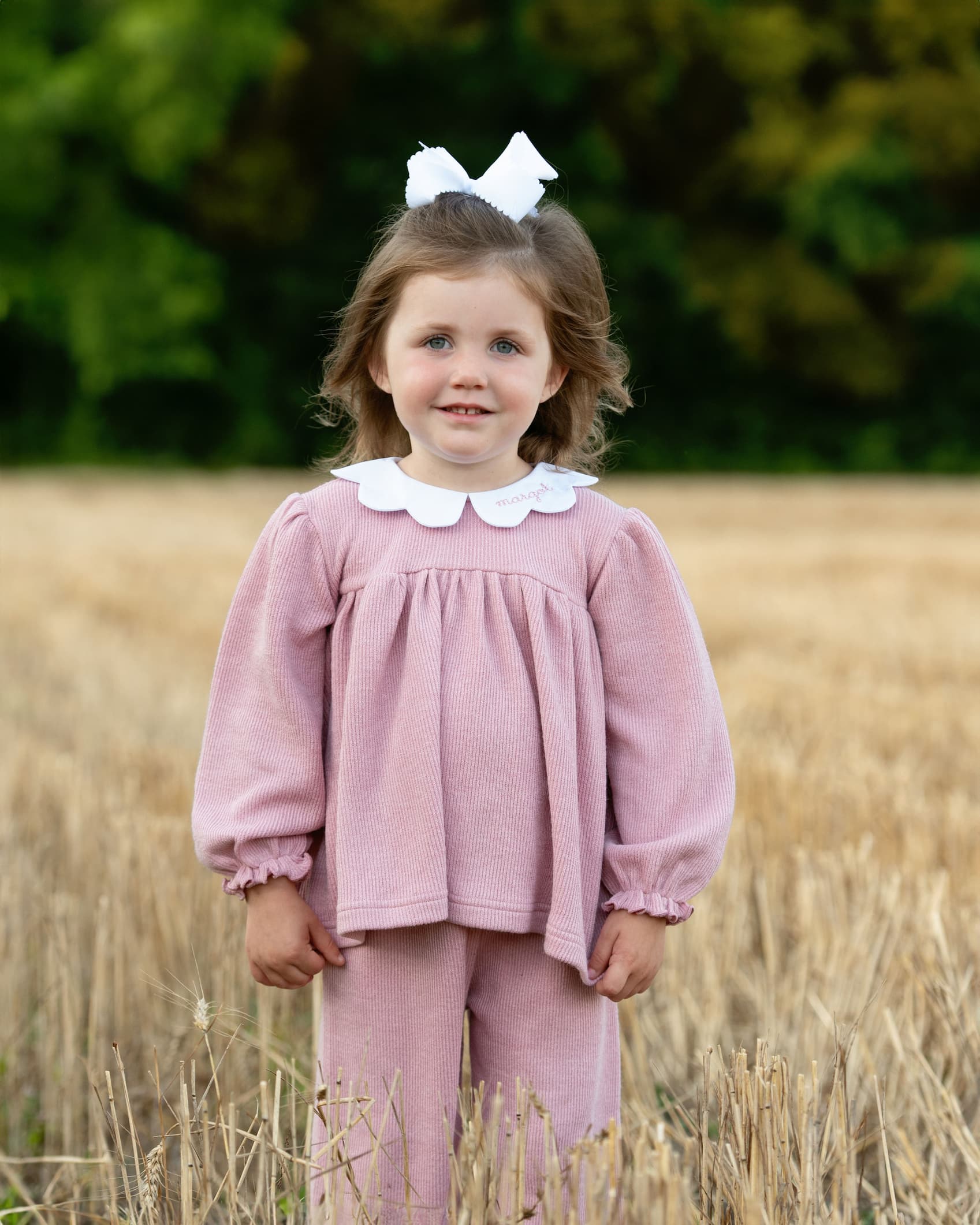 Young girl in a pink outfit standing in a field with a blurred green background