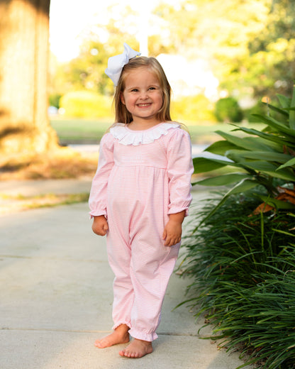 Young girl in a pink outfit standing outdoors with greenery in the background