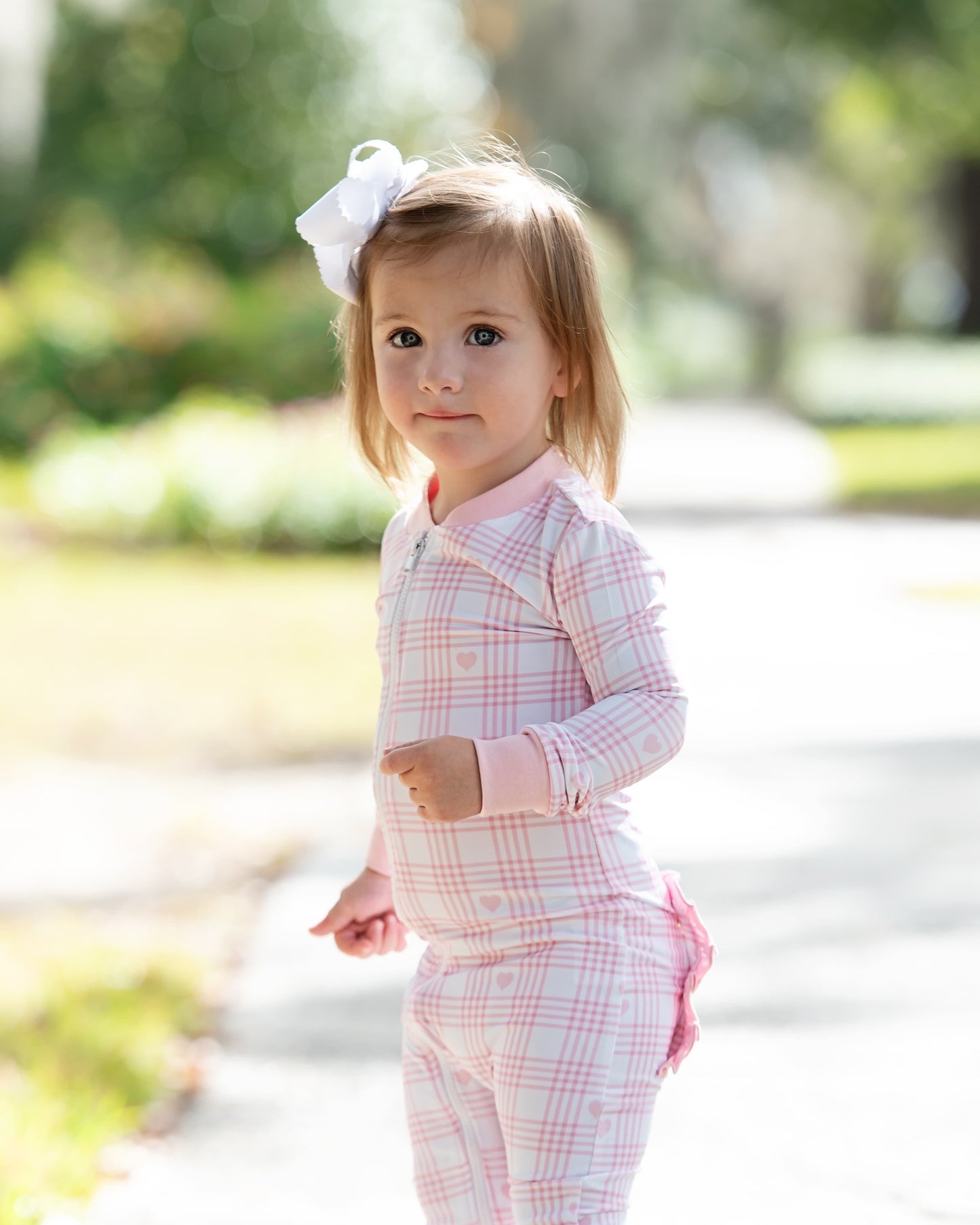 Young girl in a pink plaid outfit with a white bow outdoors