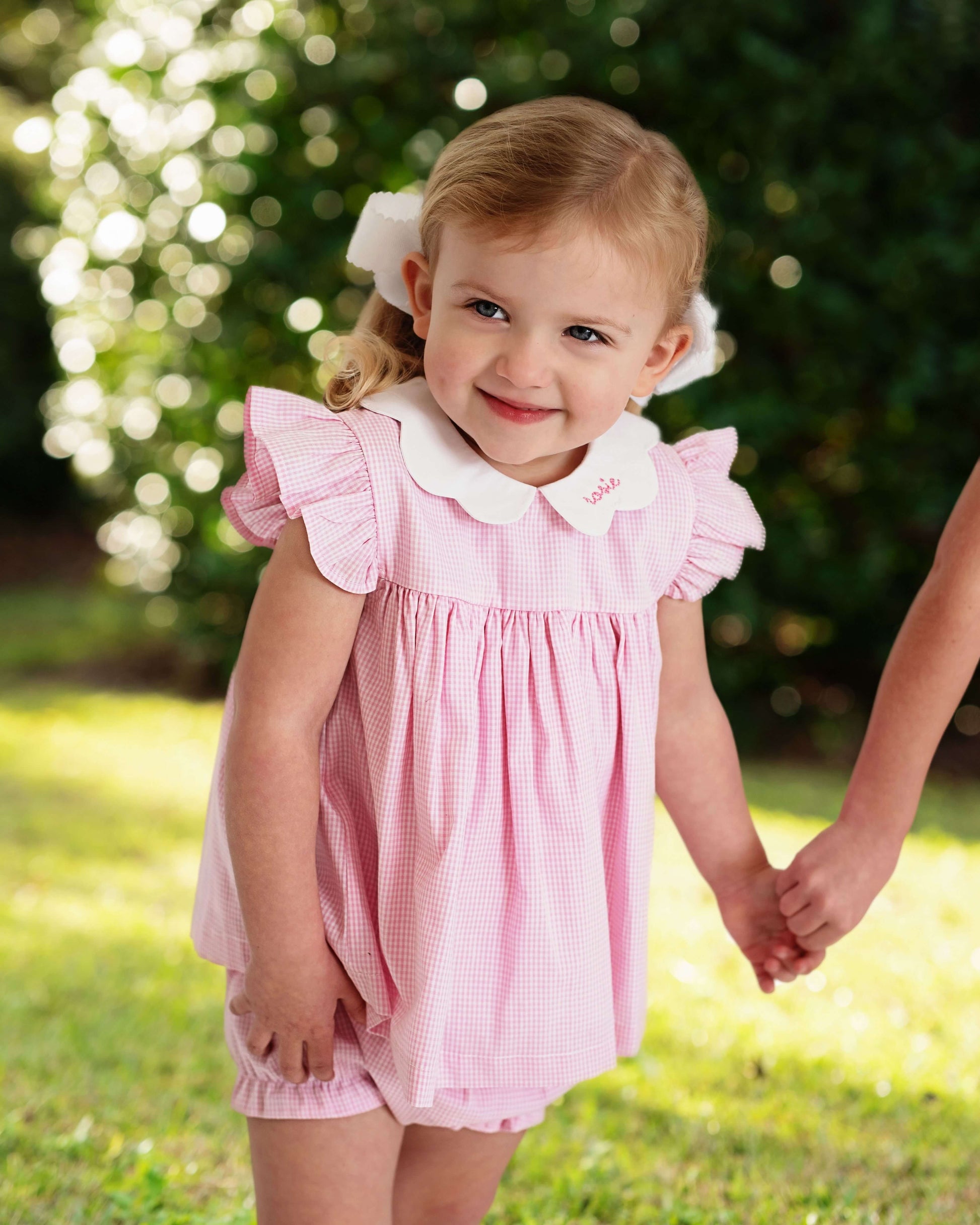 Young girl in a pink dress standing outdoors with greenery in the background
