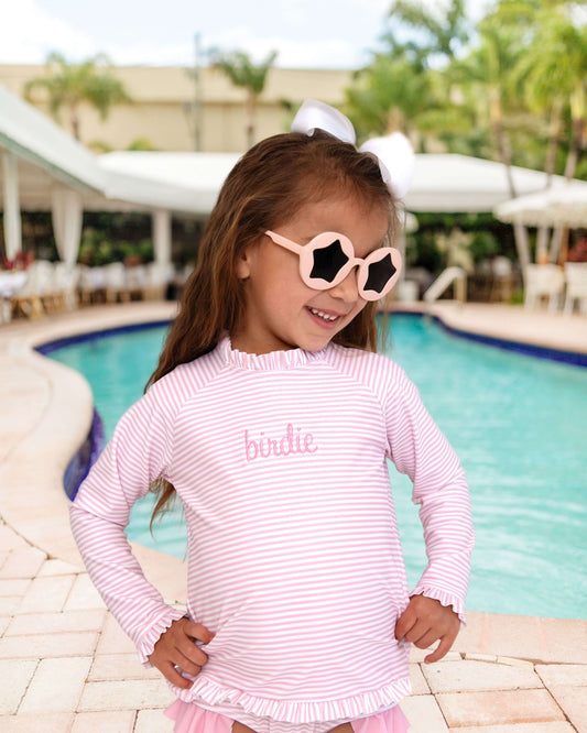 Young girl in a pink striped dress and sunglasses by a pool
