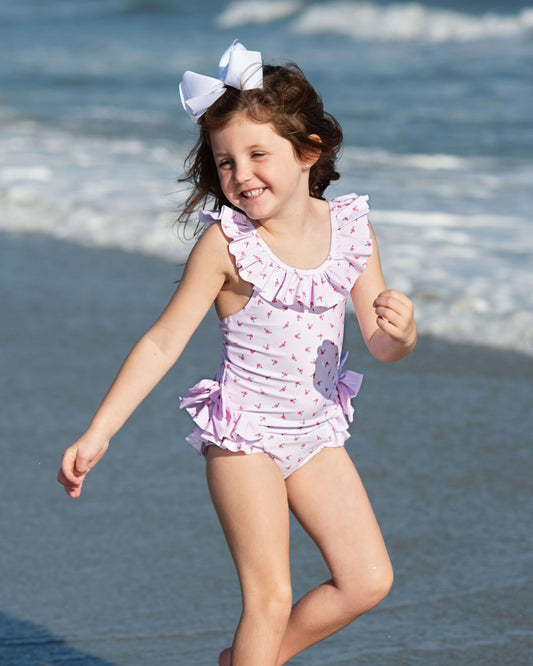 Young girl in a pink swimsuit with ruffles and a bow, standing on a beach.