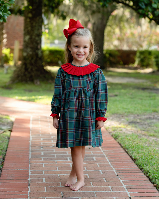 Young girl in a plaid dress with a red bow standing on a brick path.