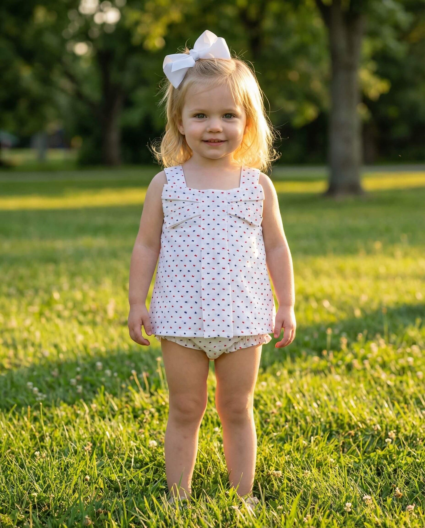 Young girl in a polka dot dress standing in a grassy field with trees in the background