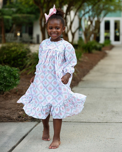 Young girl in a pumpkin night gown standing on a sidewalk with trees and bushes in the background 2