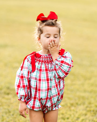 Young girl in a red and white checkered outfit with a red bow in her hair, standing in a field.