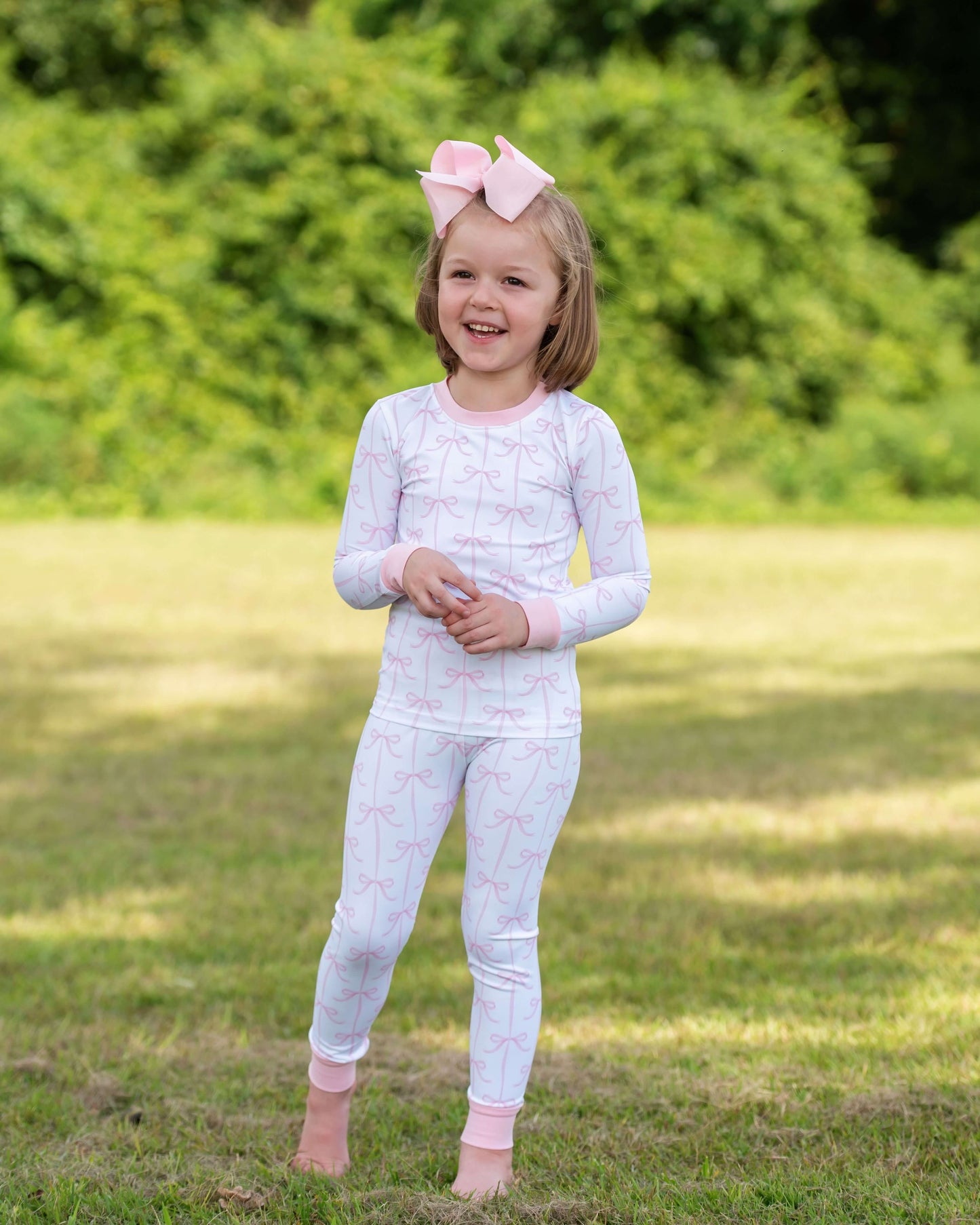 Young girl in a white checkered outfit with pink accents standing outdoors on grass.