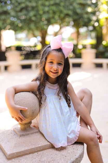Young girl in a white dress with a pink bow sitting outdoors.