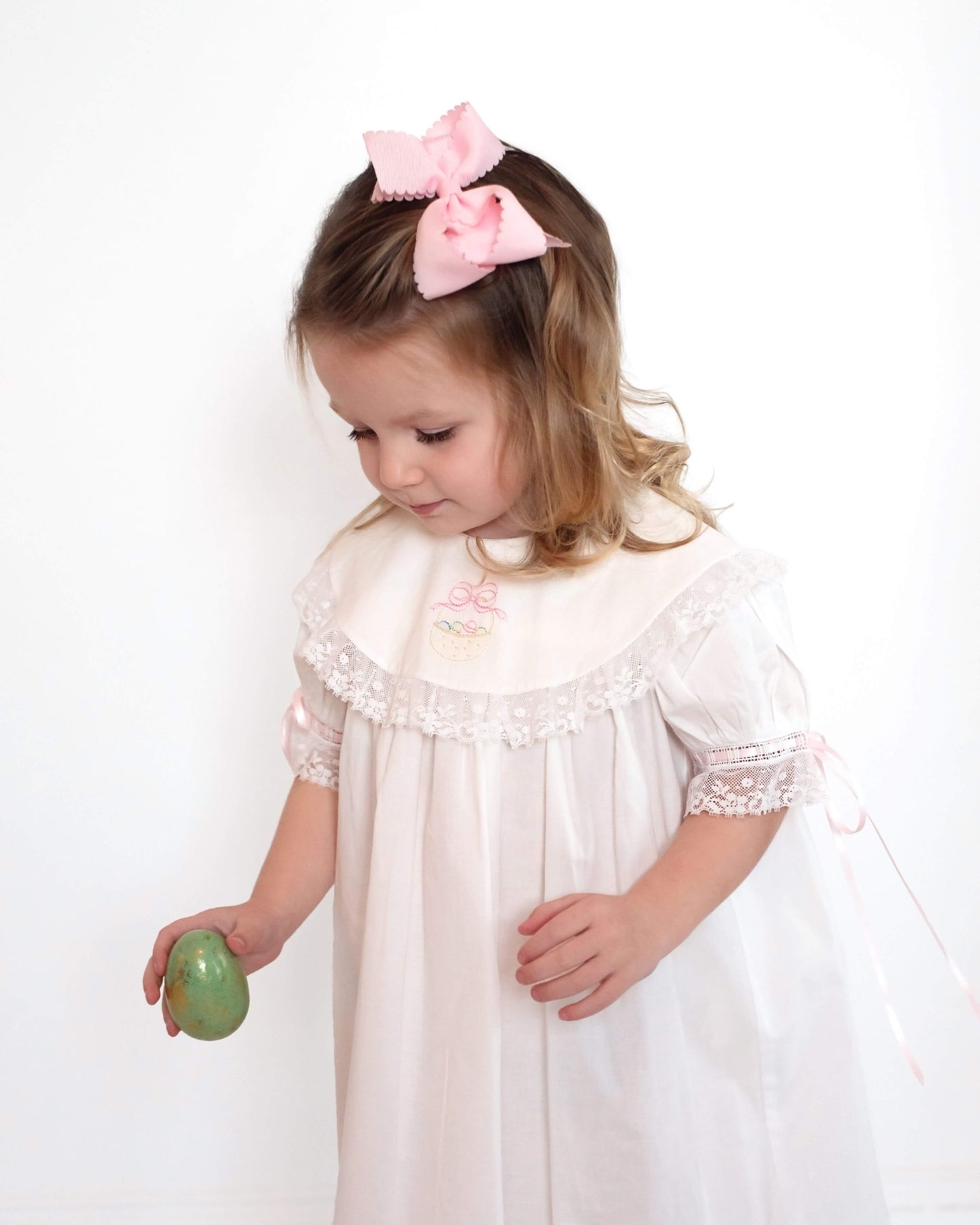 Girl wearing white embroidered Easter dress with pink ribbon ties, studio portrait