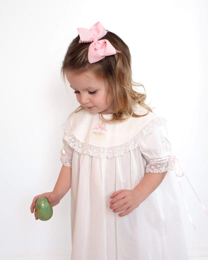 Girl wearing white embroidered Easter dress with pink ribbon ties, studio portrait