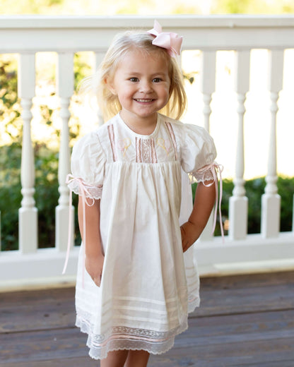 Young girl in a white dress with lace details standing on a wooden deck.