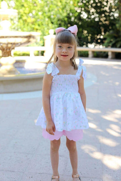 Young girl in a white dress with pink accents standing outdoors.
