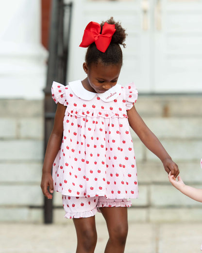 Young girl in a white dress with red polka dots and a large red bow standing outdoors.