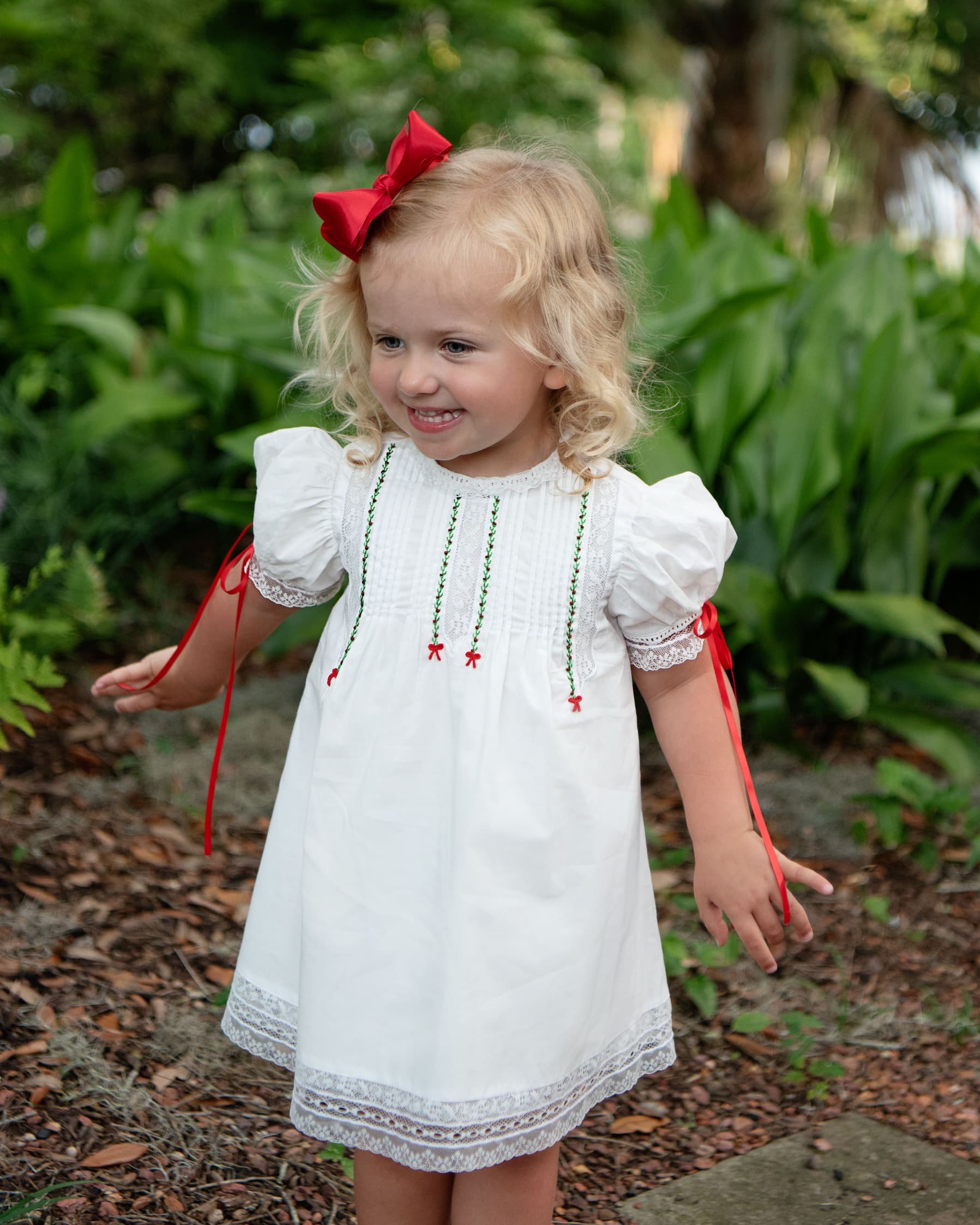 Young girl in a white dress with red ribbons and a bow outdoors