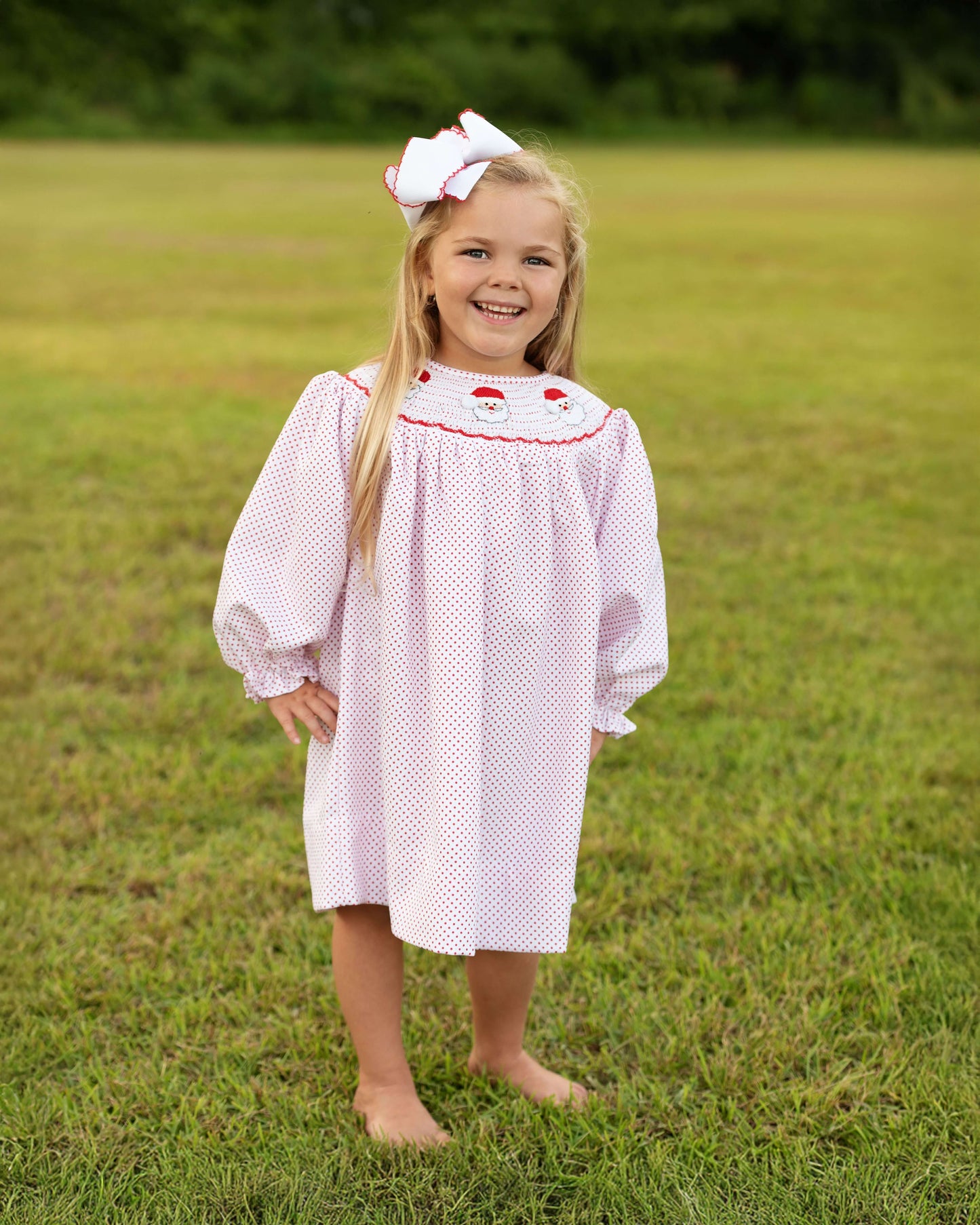 Young girl in a white dress with red trim standing in a grassy field