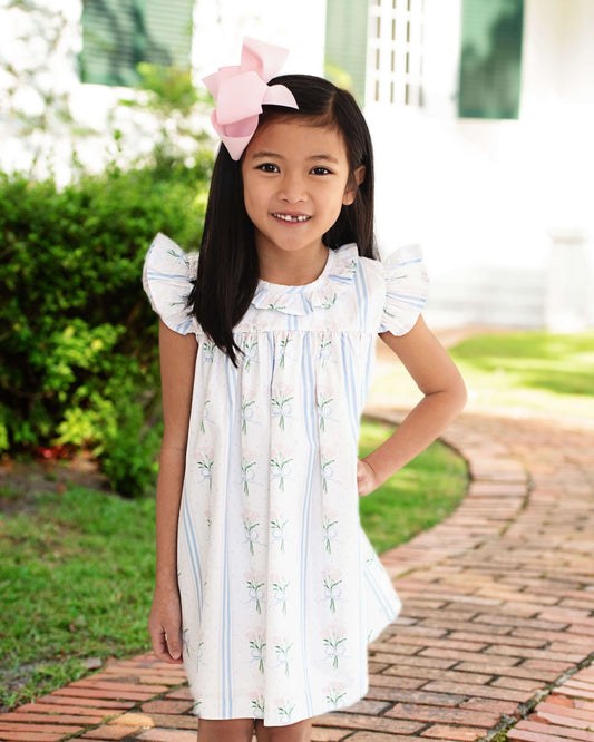 Young girl in a white dress with ruffled sleeves standing outdoors on a brick path.