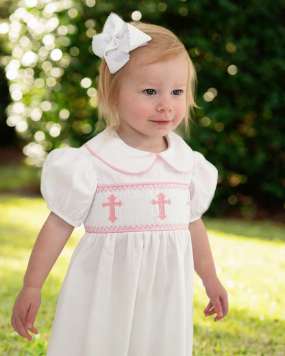 Young girl in a white dress with smocked pink cross patterns outdoors