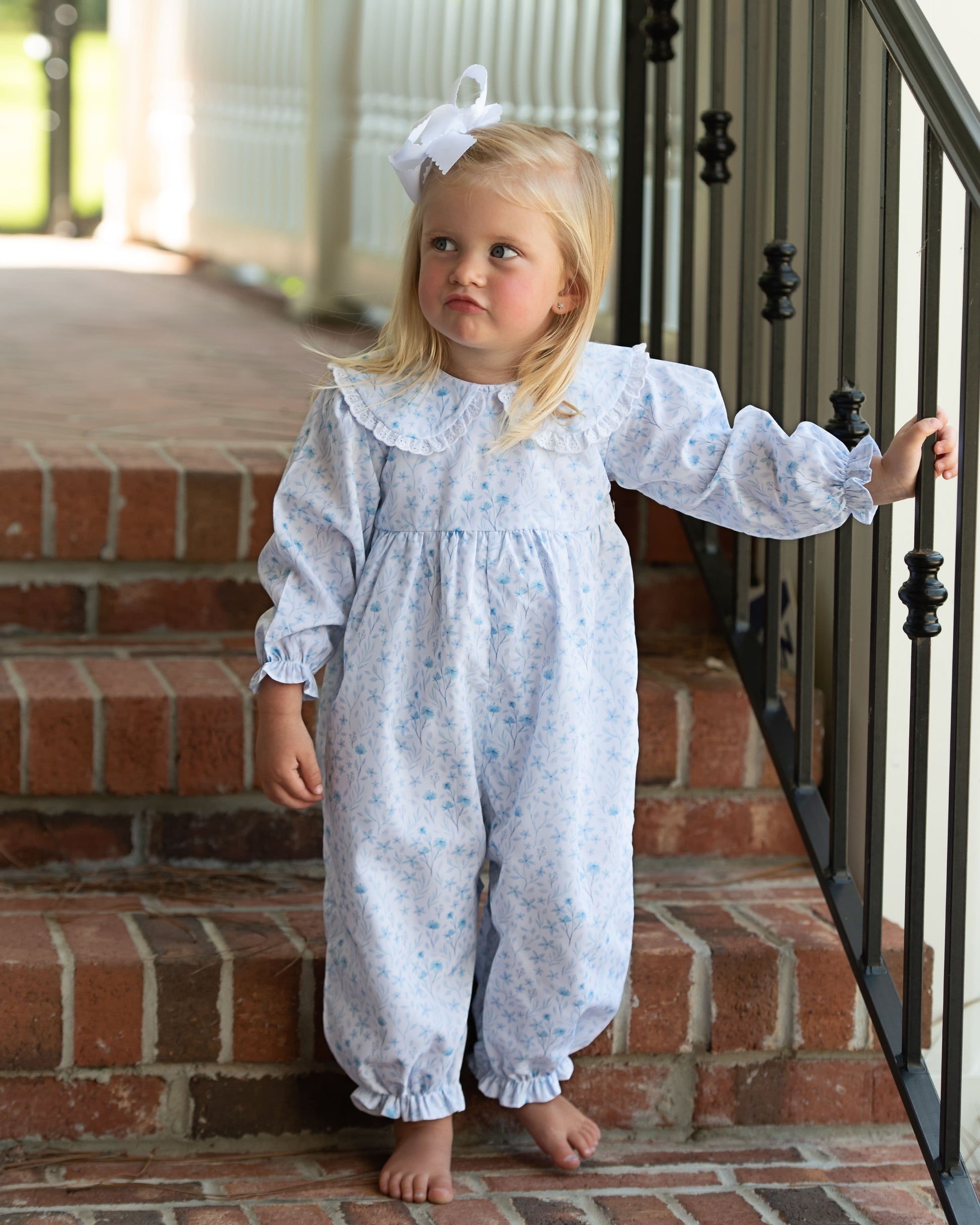 Young girl in a white floral dress standing on a brick staircase.