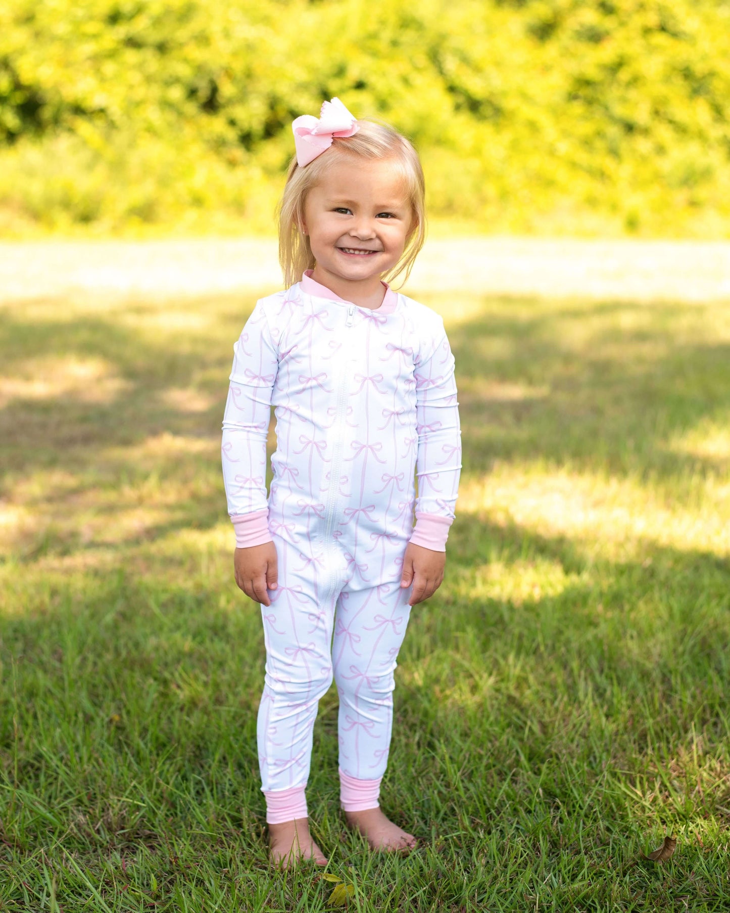 Young girl in a white outfit with pink accents standing in a grassy field.