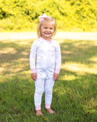 Young girl in a white outfit with pink accents standing in a grassy field.