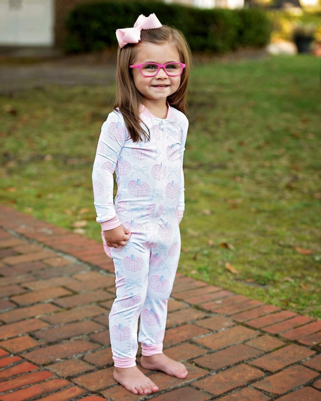 Young girl in a white outfit with pink and blue pumpkins on a brick path.