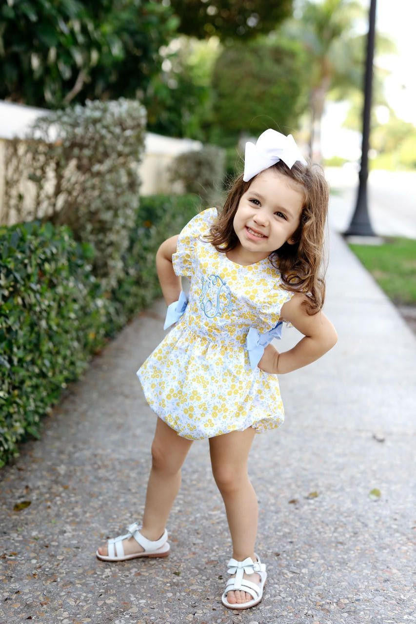 Young girl in a yellow floral bubble with blue bows standing on a path with greenery in the background