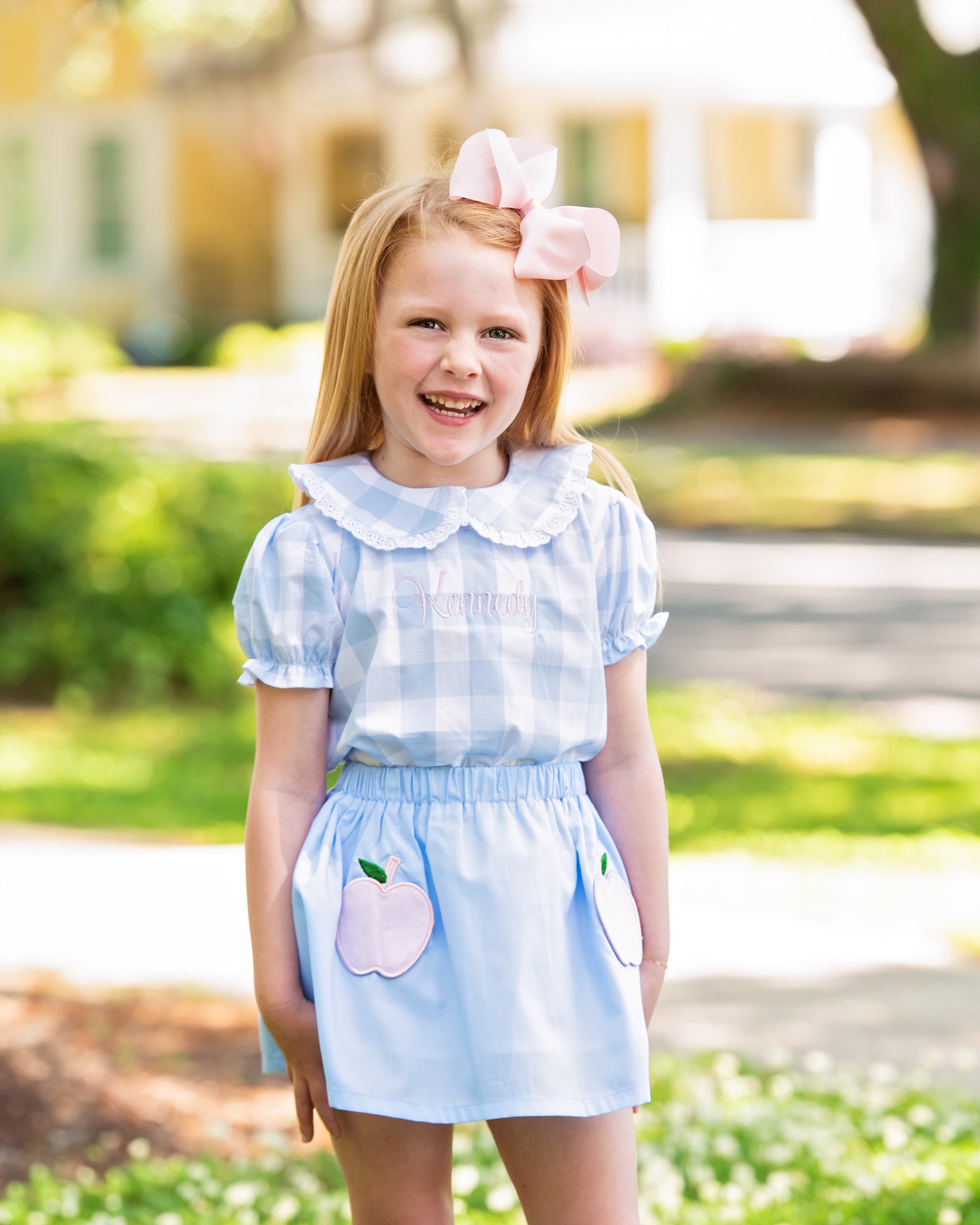 Young girl in blue outfit with apples smiling.