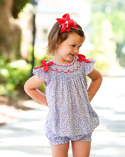 Young girl in lavender floral outfit with red bows 