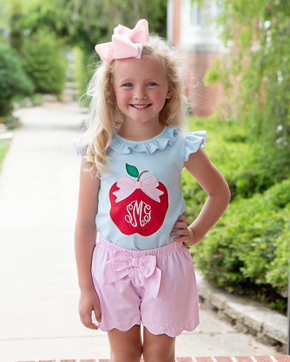 Young girl posing with hand on her hip wearing pink shorts and a shirt with an apple on it. 