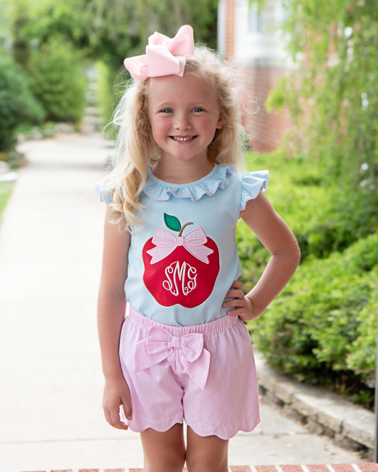 Young girl posing with hand on her hip wearing pink shorts and a shirt with an apple on it. 