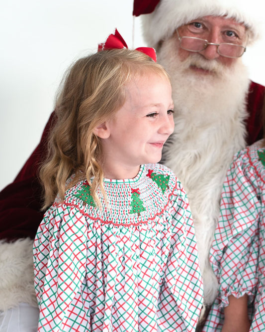 Young girl sitting with Santa Clause wearing a Christmas outfit with trees on it
