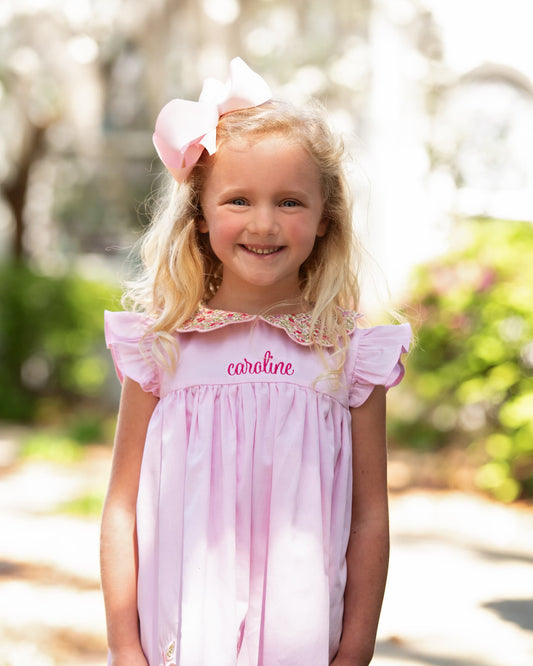 Young girl smiling wearing a pink bow and pink dress with the name caroline on it