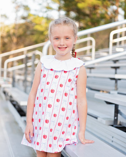 Young girl standing on bleachers wearing an apple and bow print dress.
