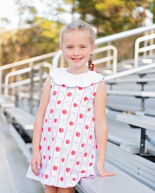 Young girl standing on bleachers wearing an apple and bow print dress.