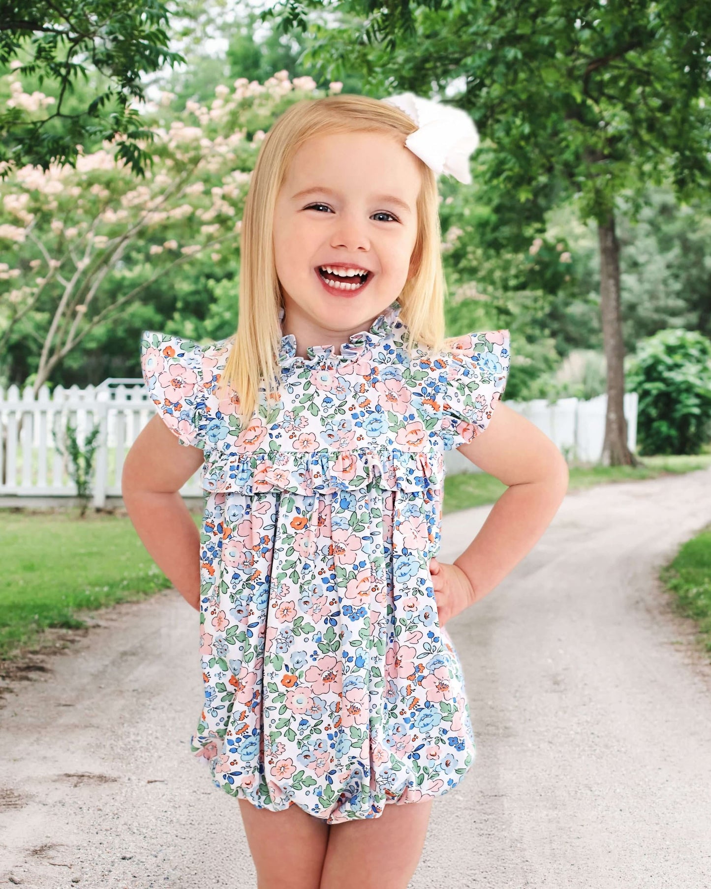 Young girl standing outside in a floral bubble, wearing a bow in her hair