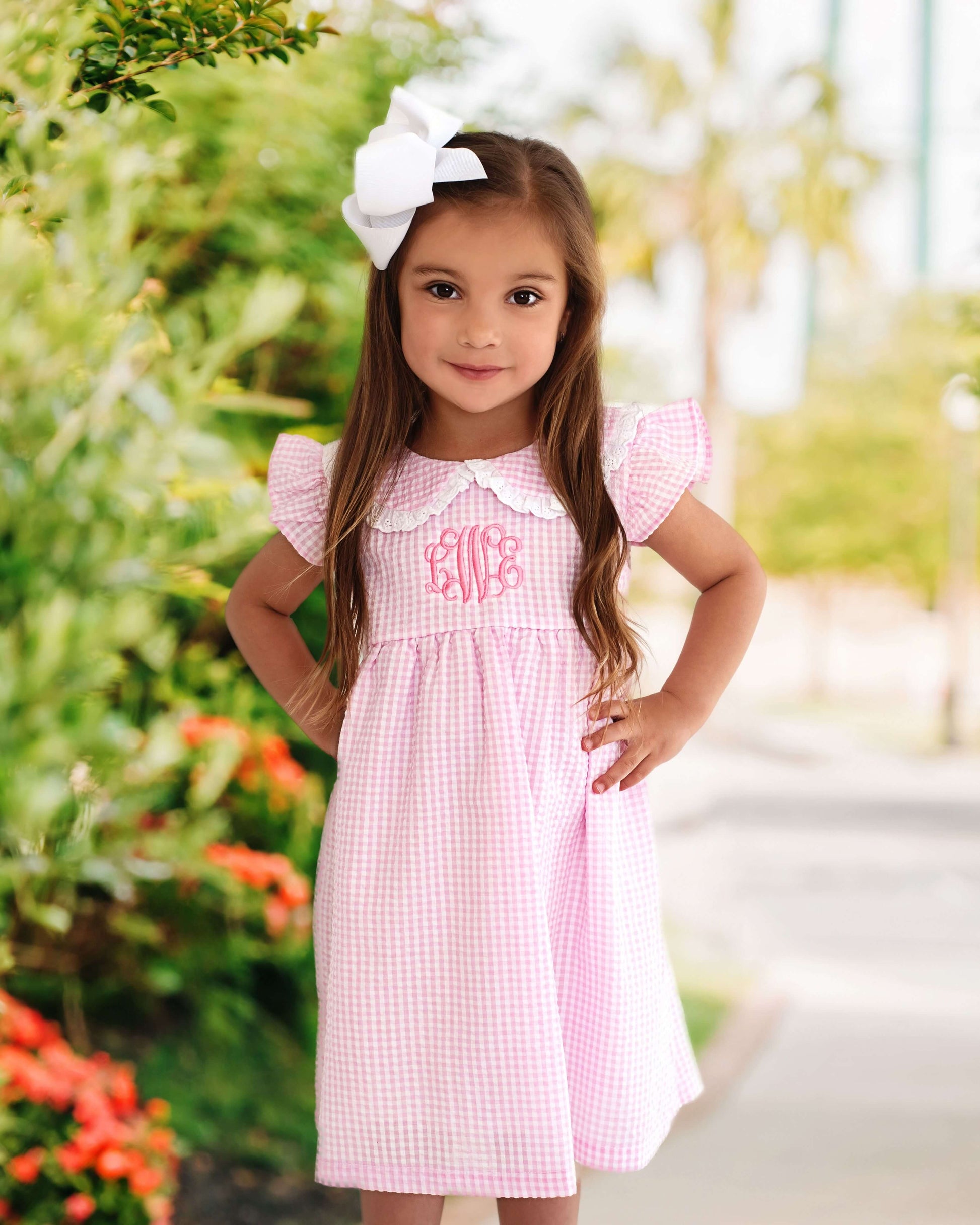 Young girl standing outside in a pink gingham dress with a white bow in her hair