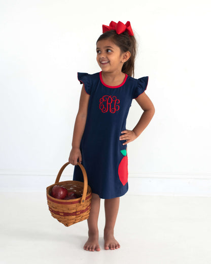 Young girl wearing a basket with apples in it wearing a navy dress with an applique apple.