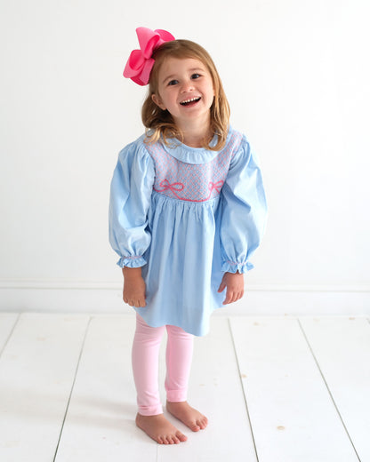 Young girl wearing a blue and pink legging set standing on a white floor.