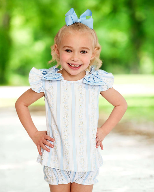 Young girl wearing a blue and white striped outfit with ruffled sleeves, standing outdoors.