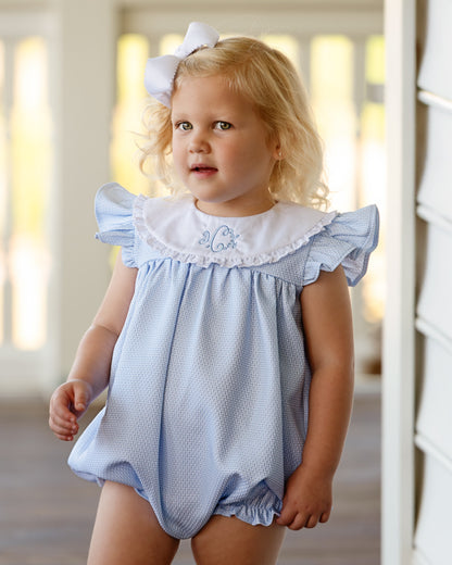 Young girl wearing a blue bubble with white ruffled collar indoors.