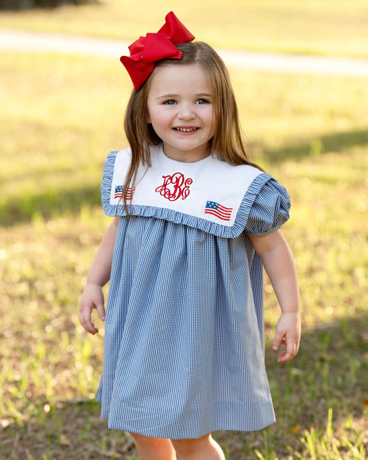 Young girl wearing a blue checkered dress with a red bow in a grassy field