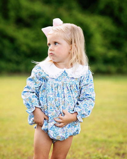 Young girl wearing a blue floral dress with a white collar outdoors.