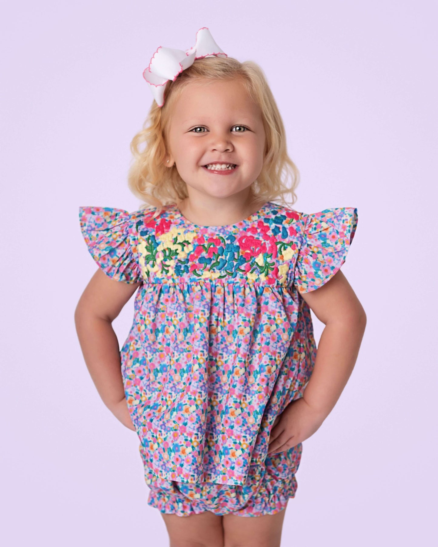 Young girl wearing a colorful floral dress against a light purple background