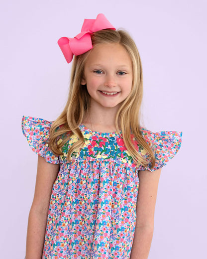 Young girl wearing a colorful floral dress with a pink bow on a light purple background