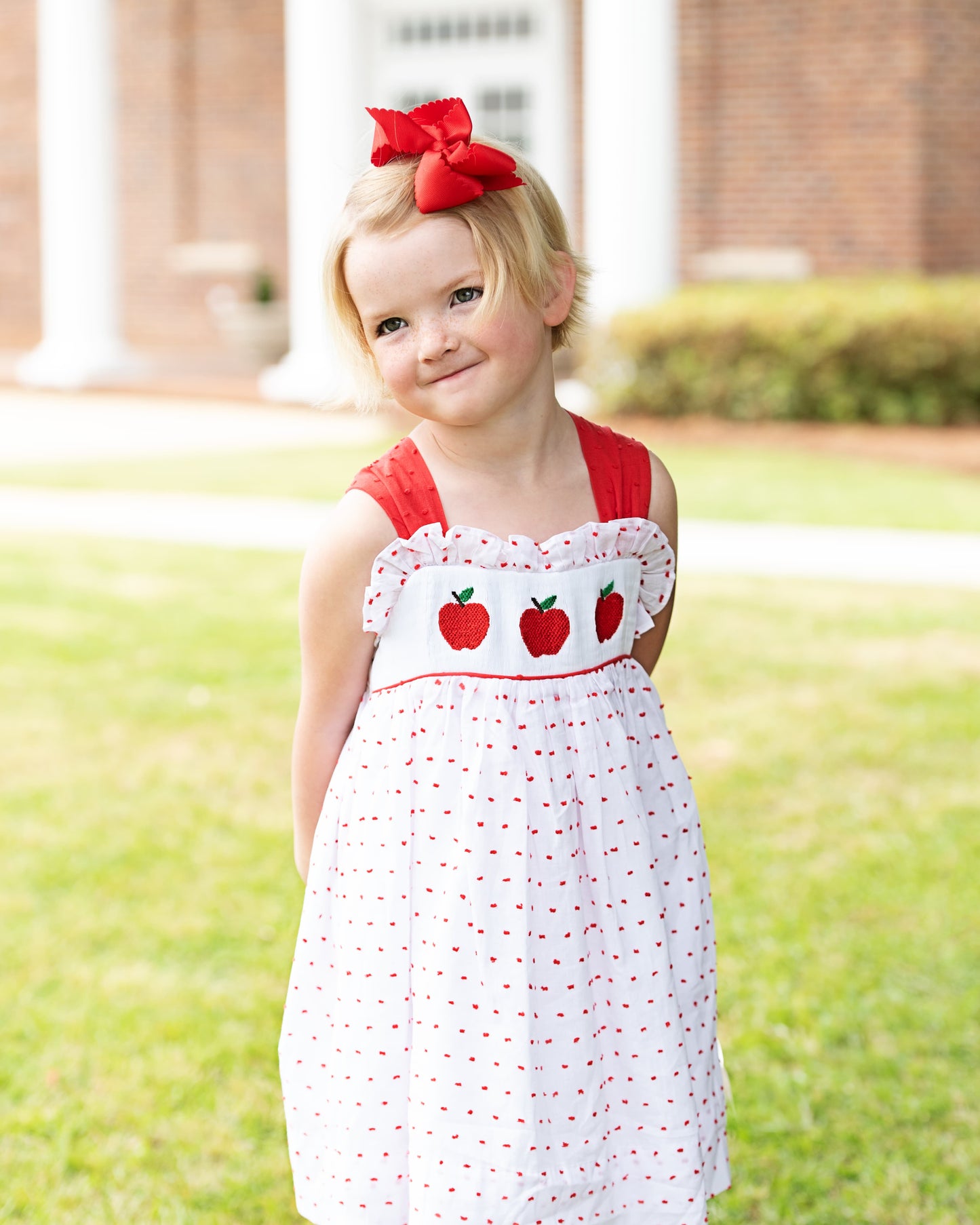 Young girl wearing a dress with smocked apples on it.