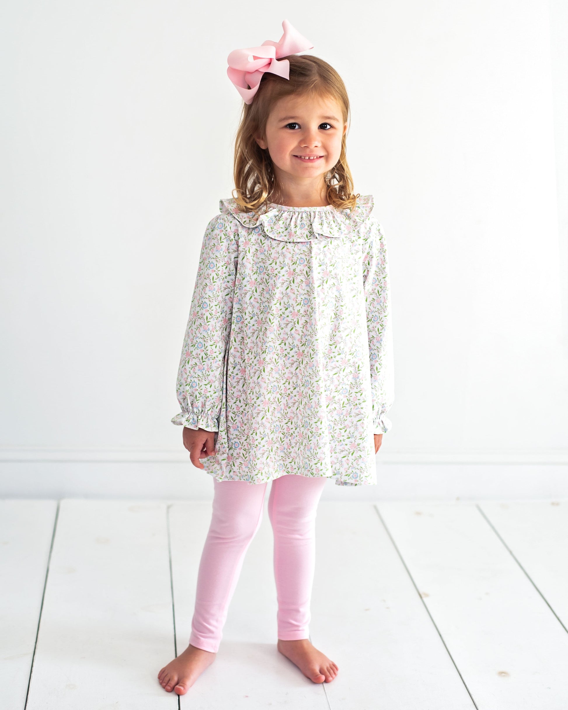 Young girl wearing a floral dress and pink leggings with a white background