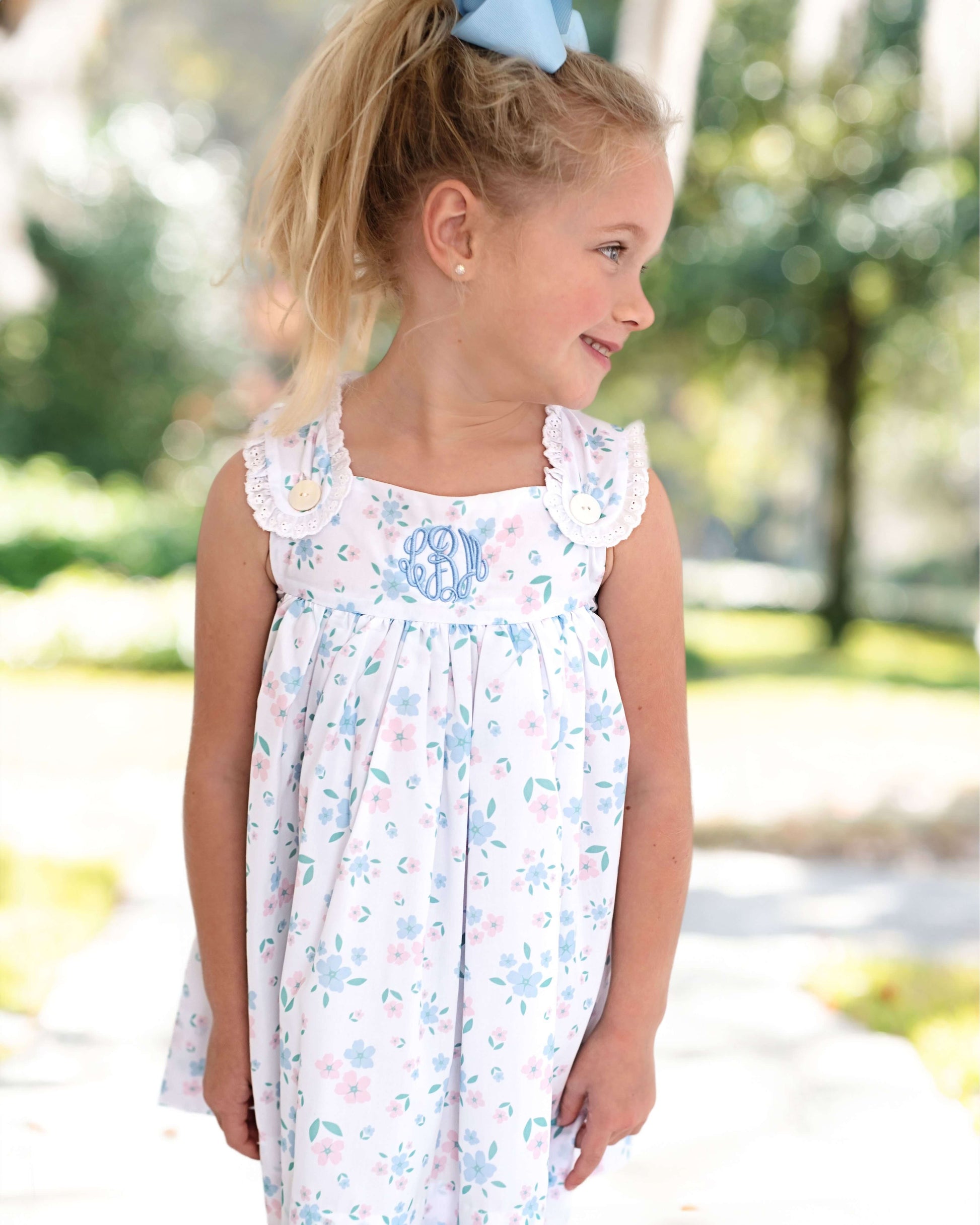 Young girl wearing a floral dress outdoors with trees in the background