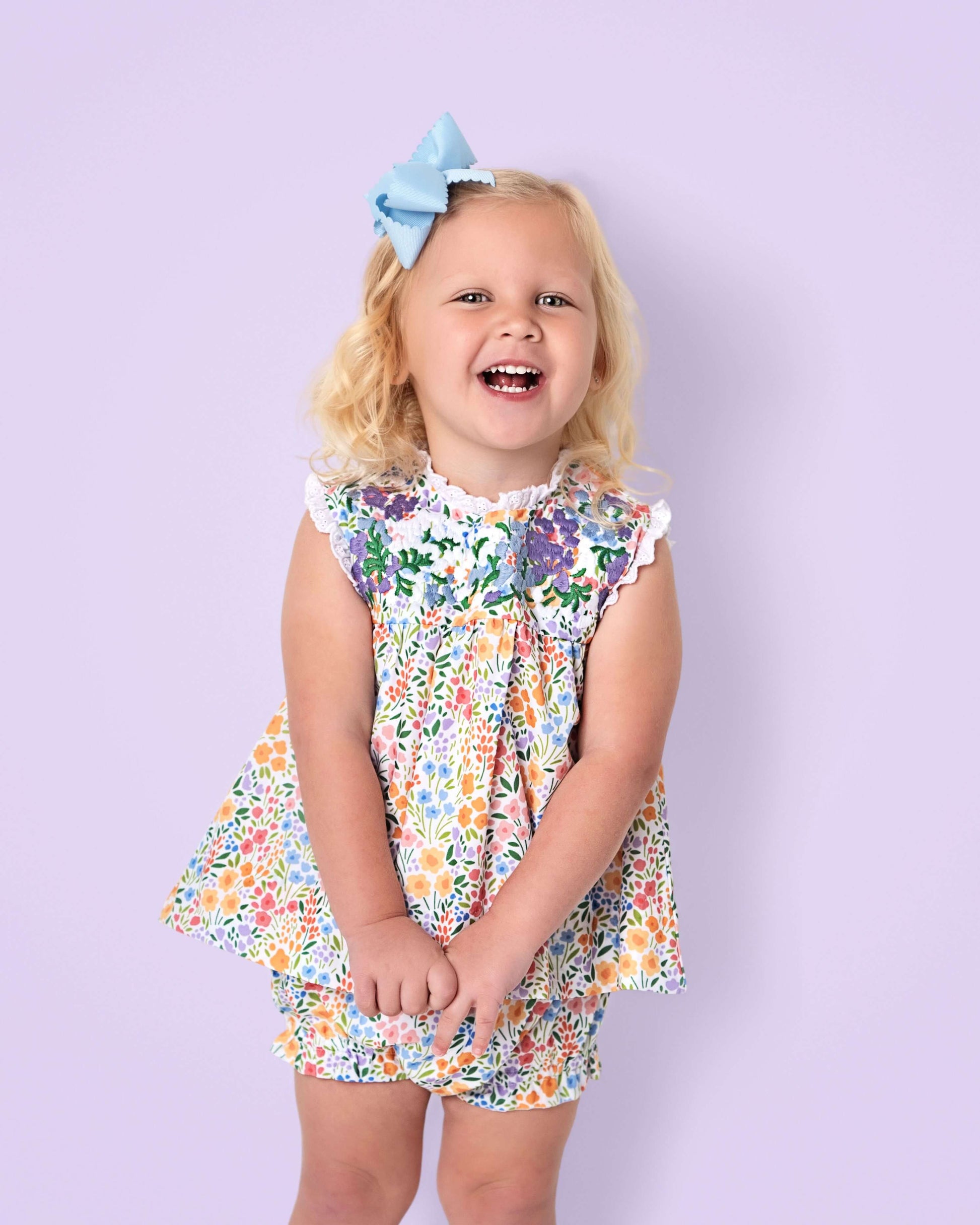 Young girl wearing a floral dress with a blue bow against a light purple background