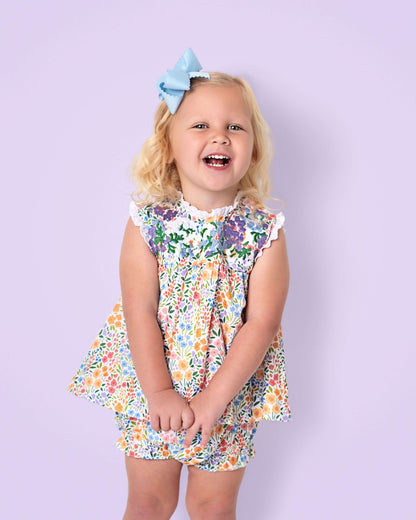 Young girl wearing a floral dress with a blue bow against a light purple background