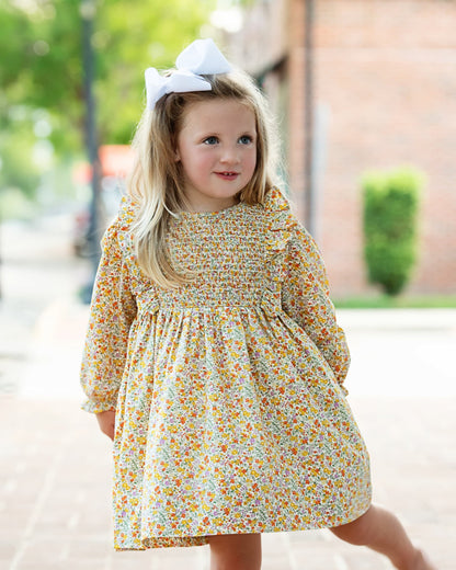 Young girl wearing a floral dress with a bow in her hair outdoors